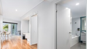 Un interior moderno con piso de madera, un baño blanco con bañera, y un balcón con vistas.