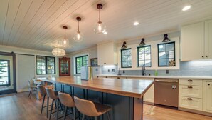 Een moderne keuken met een houten kookeiland, barstoelen, hanglampen en een vaatwasser.