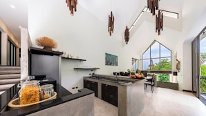 A modern kitchen with a central island, black countertops, and hanging pendant lights. - Baan Sethai (Koh Samui)