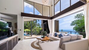 A modern living room with a large TV, a sofa, and a view of the ocean. - Baan Sethai (Koh Samui)