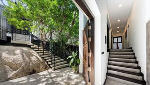 A modern staircase with a stone wall and metal railings, leading to a door with a wooden panel design. - Baan Sethai (Koh Samui)