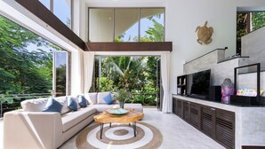 A modern living room with a sectional sofa, a wooden coffee table, and a TV on a built-in shelf. - Baan Sethai (Koh Samui)