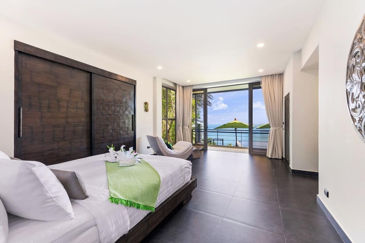 Quarto de hotel moderno com uma cama grande, área de estar e varanda com vista para o oceano.
