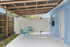 A covered patio with a table and chairs, a wooden fence, and a blue wall.
