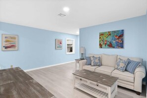 A living room with a beige sofa, a coffee table, and artwork on the walls. - Stunning Newly Renovated River District Residence (Fort Myers)
