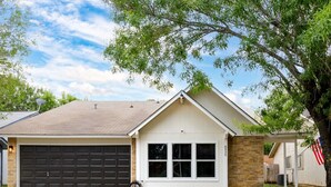 A single-story house with a garage, a front yard with a landscaped garden, and a clear sky. - Modern Retreat Near Lackland AFB  Ideal for Longer Stays (San Antonio)