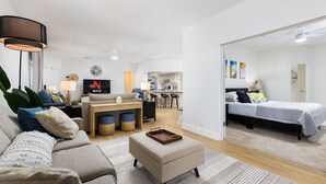 A modern living room with a sofa, ottoman, and a TV displaying the Netflix logo. - Modern Retreat Near Lackland AFB  Ideal for Longer Stays (San Antonio)