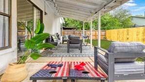 A covered patio area with outdoor furniture, a table with a red and white striped tablecloth, and a potted plant. - Modern Retreat Near Lackland AFB  Ideal for Longer Stays (San Antonio)