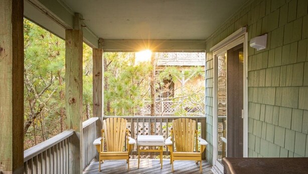 A wooden porch with two Adirondack chairs and a table, surrounded by a wooden railing and a view of trees. - Private Pool, Spa & Spacious Deck (Corolla)