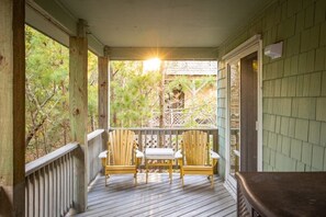 Een houten veranda met twee Adirondack-stoelen en een tafel, omringd door een houten balustrade en uitzicht op bomen.