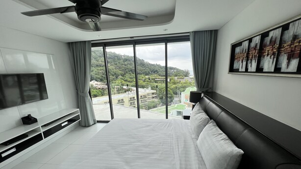 Une chambre d’hôtel moderne dotée d’un grand lit, d’un téléviseur à écran plat, d’un ventilateur de plafond et offrant une vue sur la ville grâce à de grandes fenêtres.