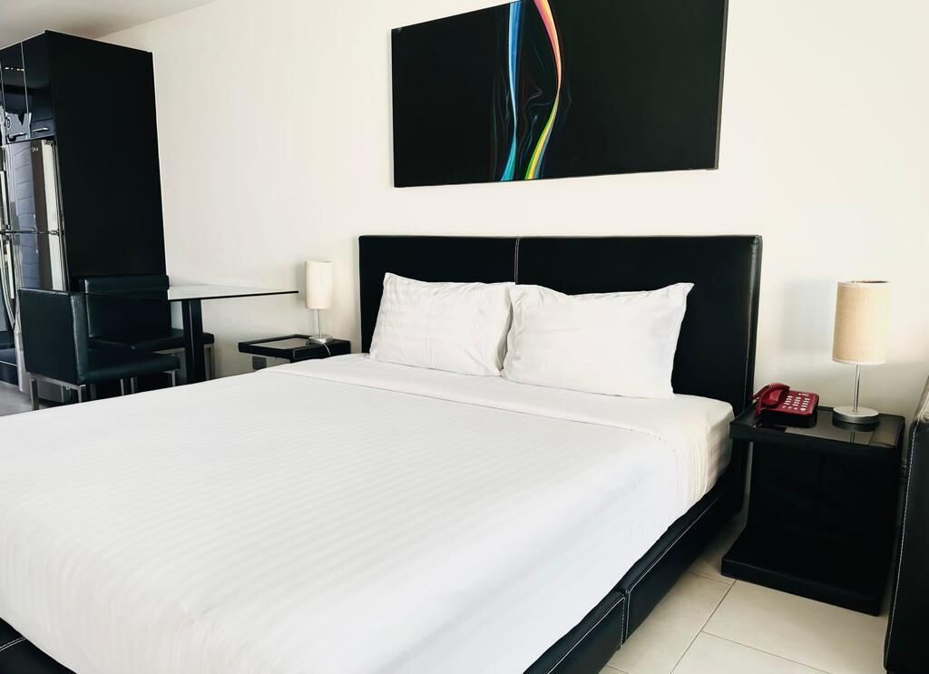 A hotel room with a large bed, a black headboard, a nightstand with a lamp and phone, and a wall-mounted abstract painting.
