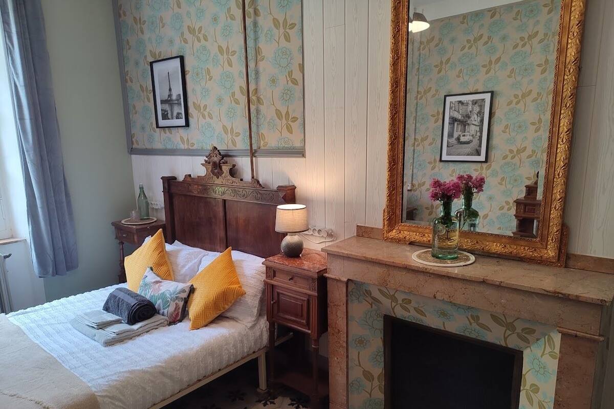 A bedroom with a bed, bedside table, lamp, and a fireplace.