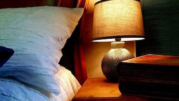 A bed with a textured white duvet, a wooden nightstand with a lamp, and a book.