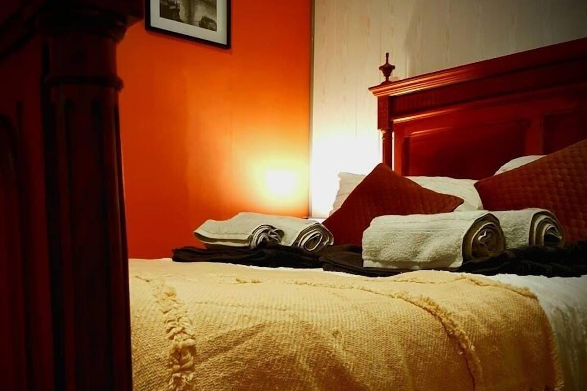 A bed with a wooden headboard, a yellow blanket, and a red pillow.