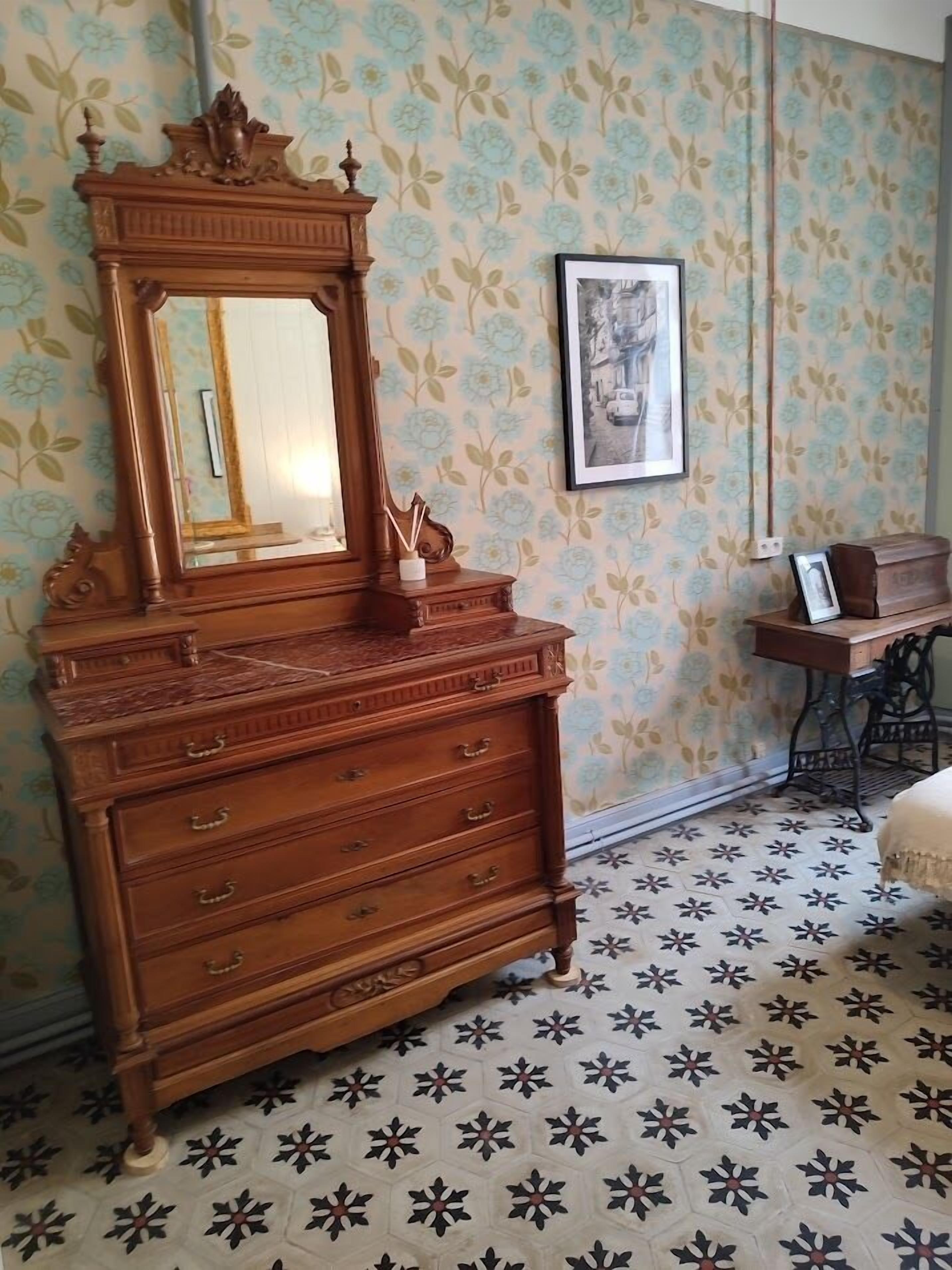 A room with a wooden dresser with a mirror, floral wallpaper, and a patterned floor.