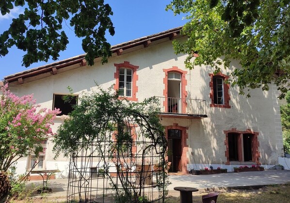 Un edificio de dos pisos con un balcón, una ventana de marco rojo y una puerta.