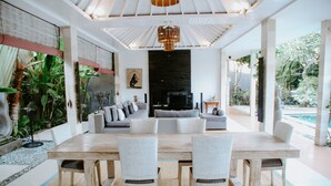 A spacious living area with a large wooden table and white wicker chairs, a grey sofa, and a black fireplace. - Villa Martini in heart of Seminyak (Seminyak)