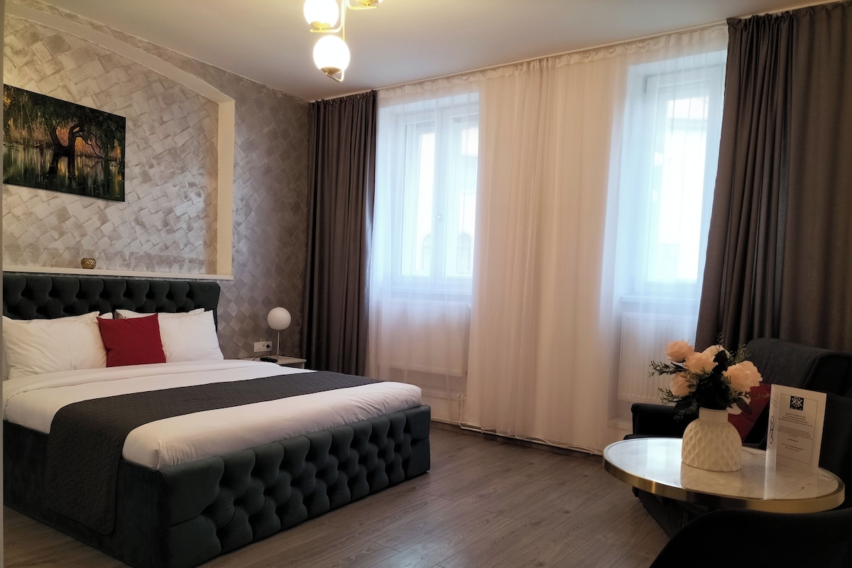 A hotel room with a large bed, a round table with a vase of flowers, and a painting on the wall.