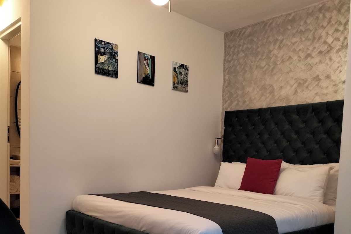 A modern bedroom with a large bed, a dark headboard, and three framed pictures on the wall.