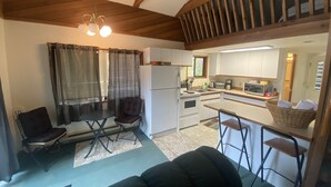 A compact kitchen with a refrigerator, stove, and microwave. There is a dining area with a table and chairs, and a sofa in the foreground. - Waterfront cozy cabin vacation home with dock (Bamfield)