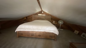 A bedroom with a wooden bed, a bedside table, a lamp, and a small shelf. - Waterfront cozy cabin vacation home with dock (Bamfield)