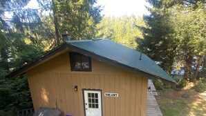 A small wooden cabin with a metal roof, a white door, and a sign reading "THE LOFT". - Waterfront cozy cabin vacation home with dock (Bamfield)