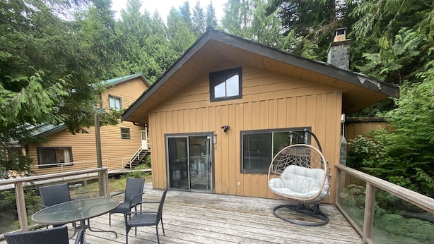 A wooden deck with a glass door, a hanging chair, and a table with chairs. - Waterfront cozy cabin vacation home with dock (Bamfield)