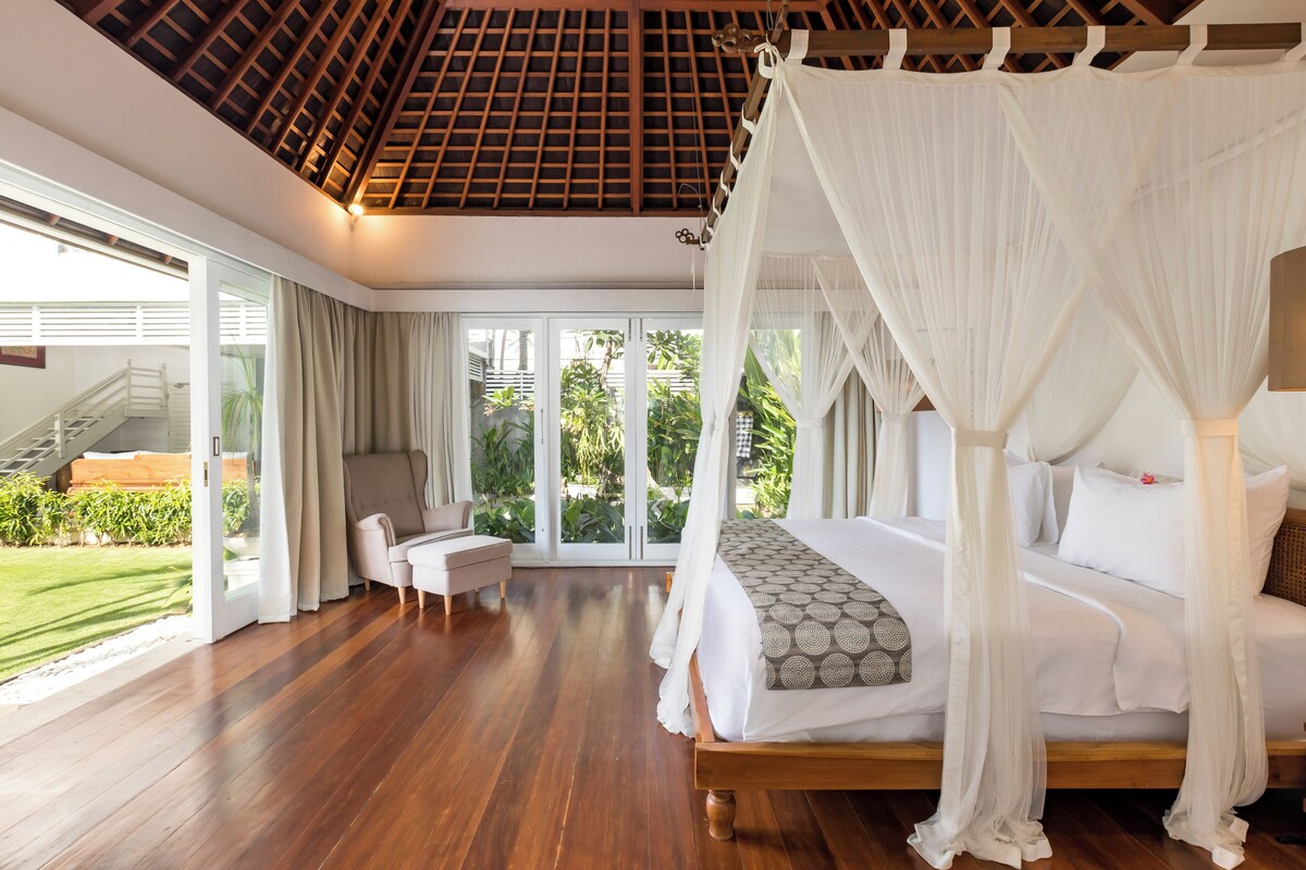 A spacious bedroom with a large bed, a sitting area, and a view of the outdoors.