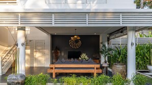 A modern outdoor seating area with a wooden bench, a TV screen, and a decorative wall hanging. - Kerta Rama Seminyak (Keroboken Kelod)