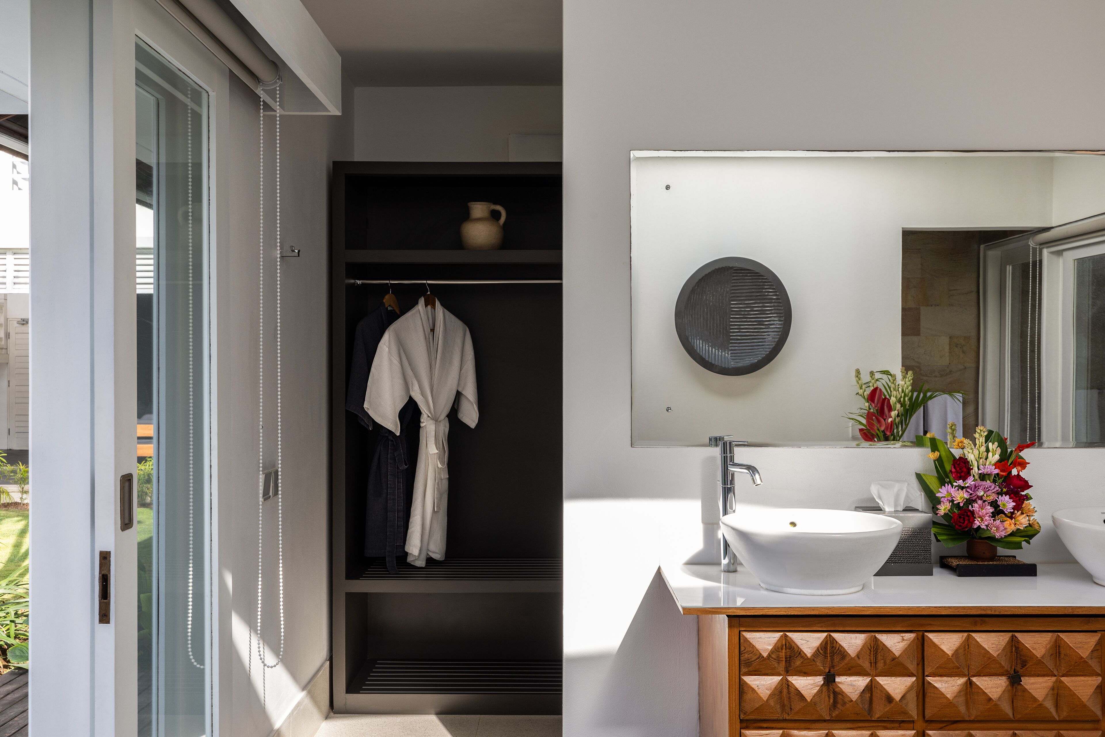 Een moderne badkamer met een witte wastafel, een grote spiegel en een houten kast.
