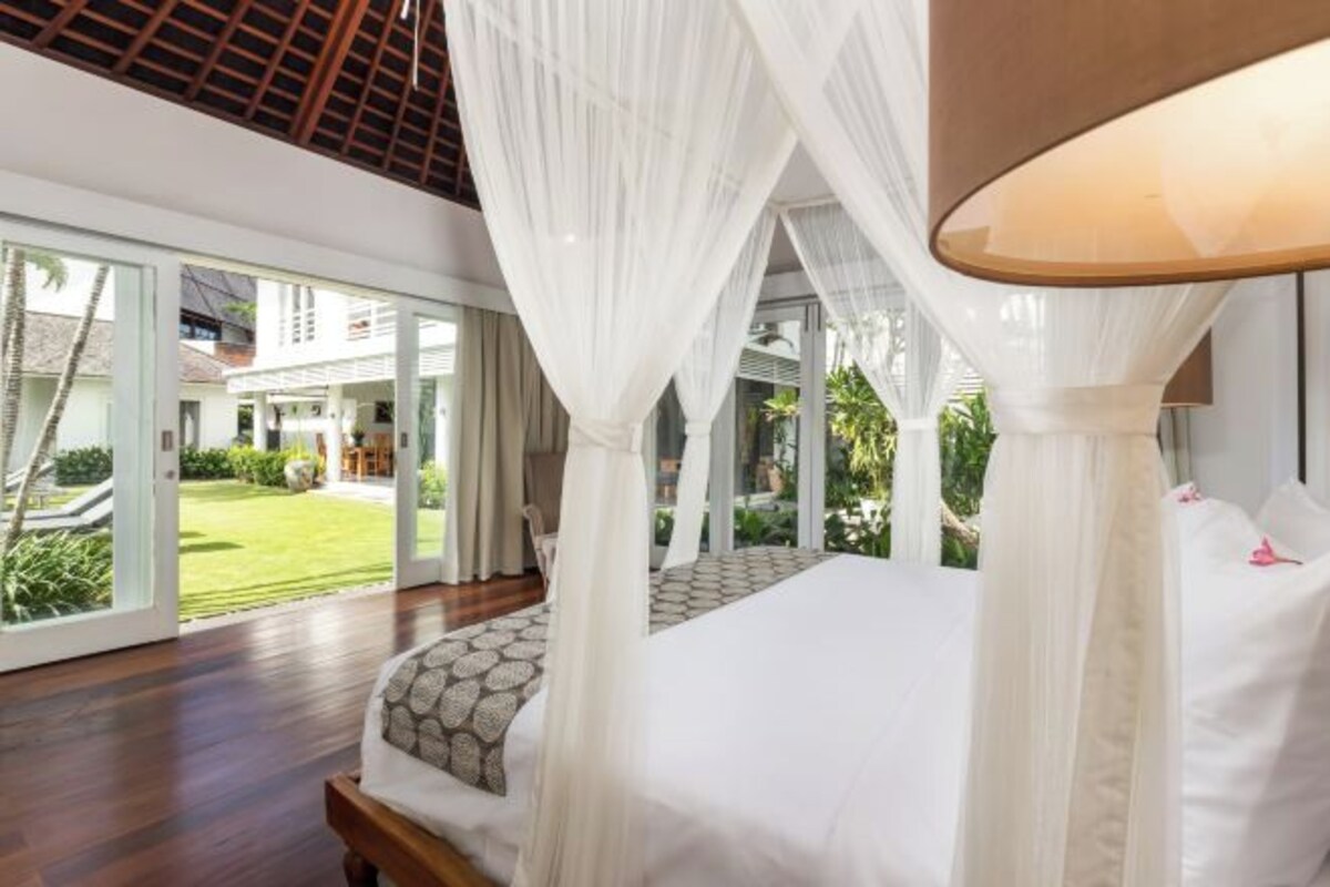 A bedroom with a canopy bed, large windows, and a view of a garden.