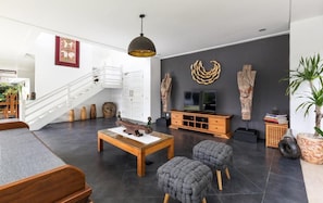 A modern living room with a staircase, a wooden coffee table, and a TV on a wooden stand. - Kerta Rama Seminyak (Keroboken Kelod)