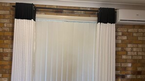 A room with a brick wall, a window with white curtains, and an air conditioning unit.
