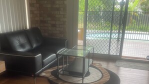 A living room with a black leather sofa, a glass coffee table, and a wooden floor.