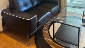 A modern living room with a black leather sofa, a glass coffee table, and a brick wall.