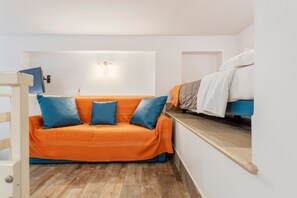 A compact room with a sofa, a bed, a desk, and a wall-mounted light fixture.