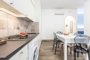 A compact kitchen with a gas stove, a washing machine, and a dining area with a table and chairs.