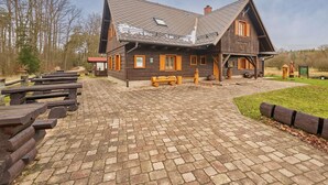 A wooden lodge with a sloped roof, a covered porch, and a paved entrance area with benches.
