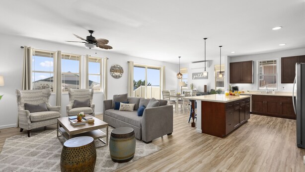 A spacious living area with a sofa, chairs, a coffee table, and a dining table. There is a kitchen area with cabinets and a refrigerator.