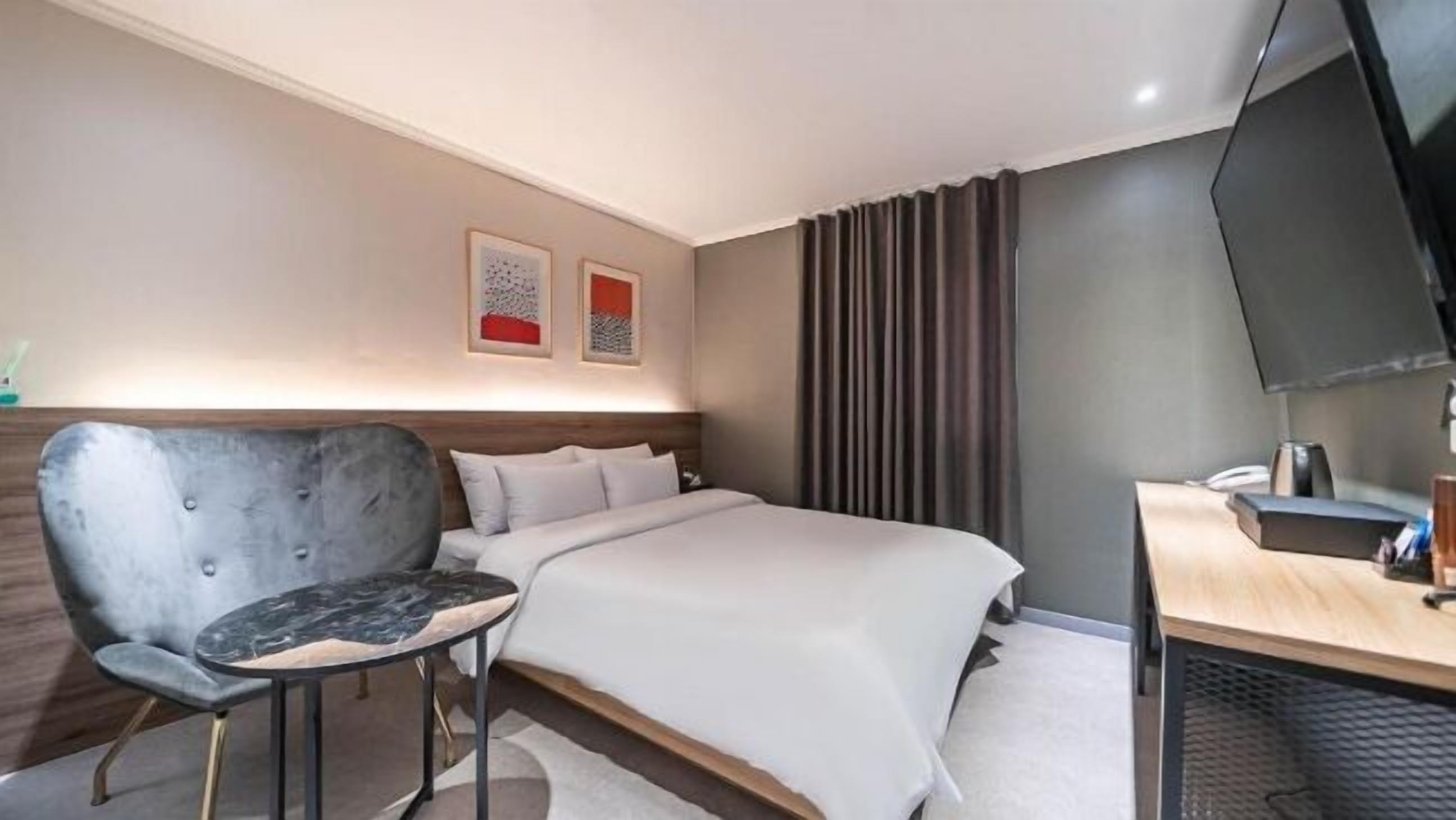 Una camera d'albergo con un letto, una sedia, una scrivania, una televisione e due quadri appesi al muro.