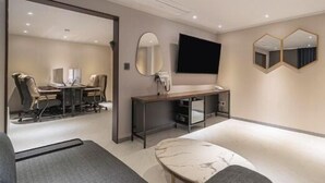 A hotel room with a desk, a flat-screen TV, a mirror, and a seating area with a sofa and a chair. - Hotel Gate (Incheon)