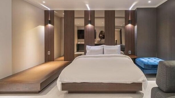 A modern bedroom with a large bed, built-in benches, and a blue ottoman. - Hotel Gate (Incheon)