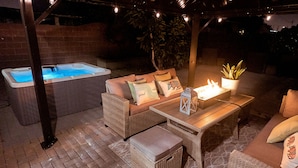 An outdoor patio area with a hot tub, wicker furniture, and a small table with a candle. - Modern Retreat w/ Private Spa, Arcade, Playground, Disney, Convention & Beaches (Anaheim)