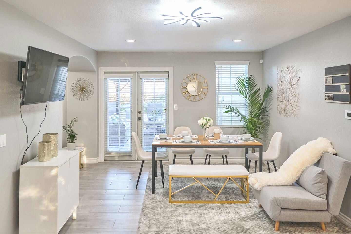 A dining area with a table set for four, a sofa, and a TV mounted on the wall.