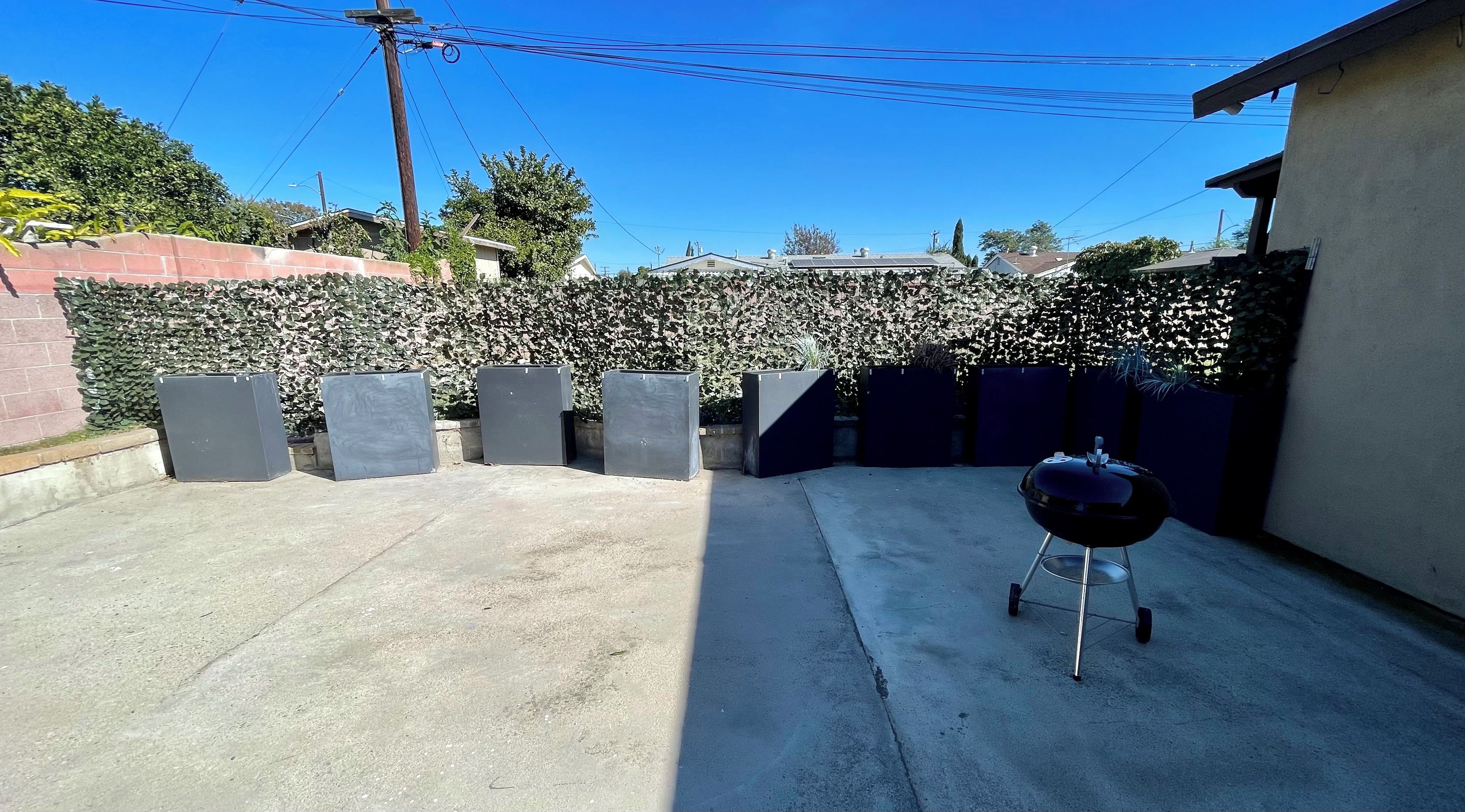 Un cortile con un barbecue, un patio in cemento e un siepe.