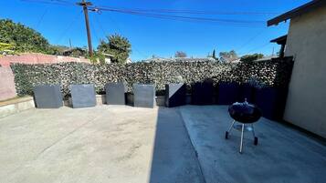 A backyard with a barbecue grill, a concrete patio, and a hedge.
