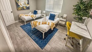A bedroom with two beds, a desk, a chair, a ceiling fan, a window with blinds, a painting, and a plant. - Modern Retreat w/ Private Spa, Arcade, Playground, Disney, Convention & Beaches (Anaheim)