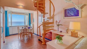 A room with a spiral staircase, a dining area with a view of the sea, and a painting on the wall. - Il Bijou Di Rossella - Beach Front Duplex With Balcony (Alassio)