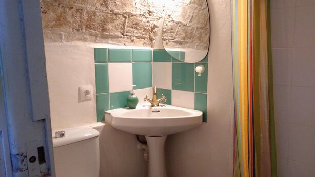 Une salle de bain avec un lavabo, un robinet et un mur recouvert de carreaux verts.